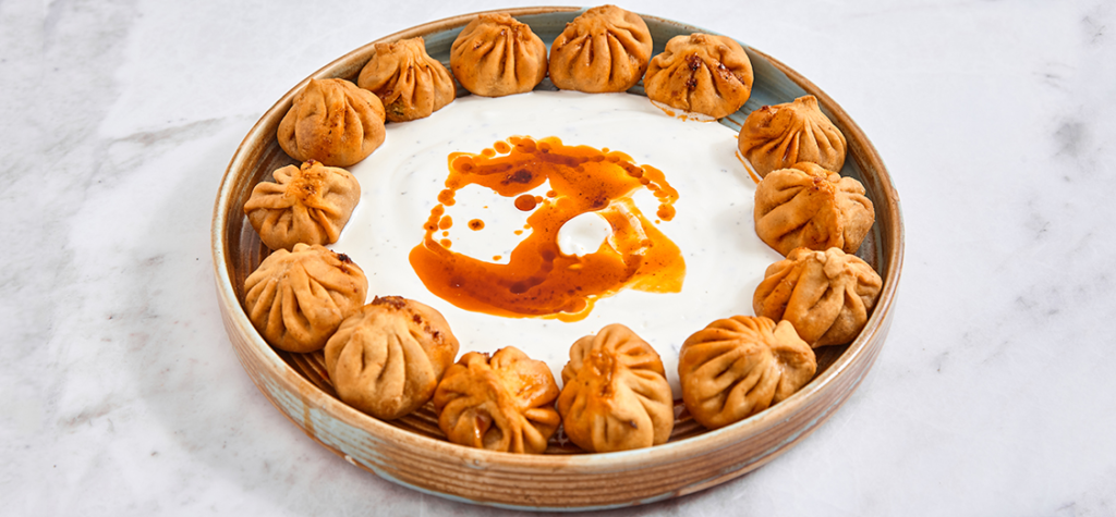 A plate of vegan dumplings arranged in a circle around a creamy yogurt dip, garnished with a drizzle of spicy oil.