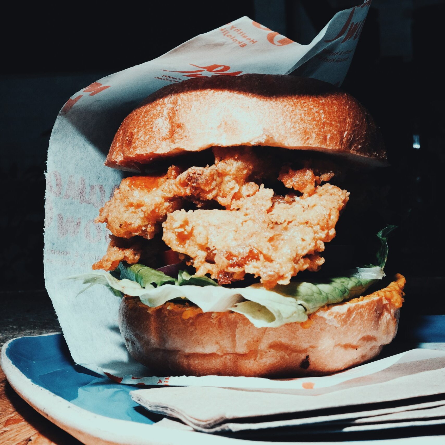 A close-up of a vegan burger with crispy fried patty, lettuce, and a toasted bun, served on a blue plate.